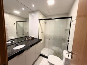 Une salle de bain moderne avec une douche à parois de verre, des toilettes blanches et un plan de toilette noir doté de deux vasques.