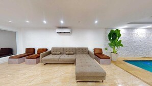 A modern living room with a sectional sofa, a potted plant, and a pool. - Modern 3BR Apt  AC + Comfort & Style (Trujillo Alto)