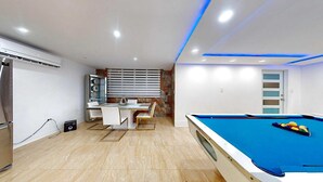 A modern room with a pool table, a dining area, and a built-in air conditioning unit. - Modern 3BR Apt  AC + Comfort & Style (Trujillo Alto)
