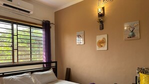 Une chambre à coucher avec un lit, une fenêtre avec des rideaux, un climatiseur fixé au mur et une table de chevet avec une lampe.