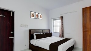 Un dormitorio con cama, ventana con cortinas, una puerta y enchufes en la pared.