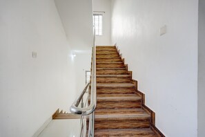 A staircase with wooden steps and a metal handrail, leading to a landing with a window. - Deluxedap Service Apartment (Chennai)