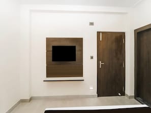 Una habitación con televisión montada, una puerta de madera y una pared blanca.