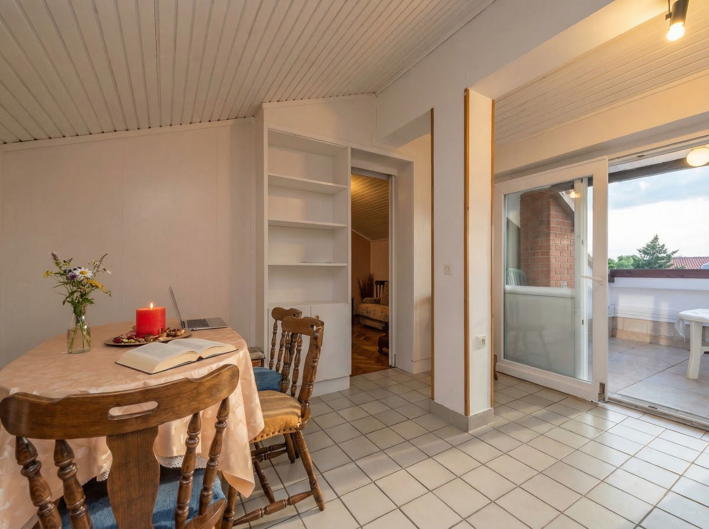 Un coin repas avec une table ronde, des chaises, un vase avec des fleurs, une bougie allumée et un ordinateur portable.