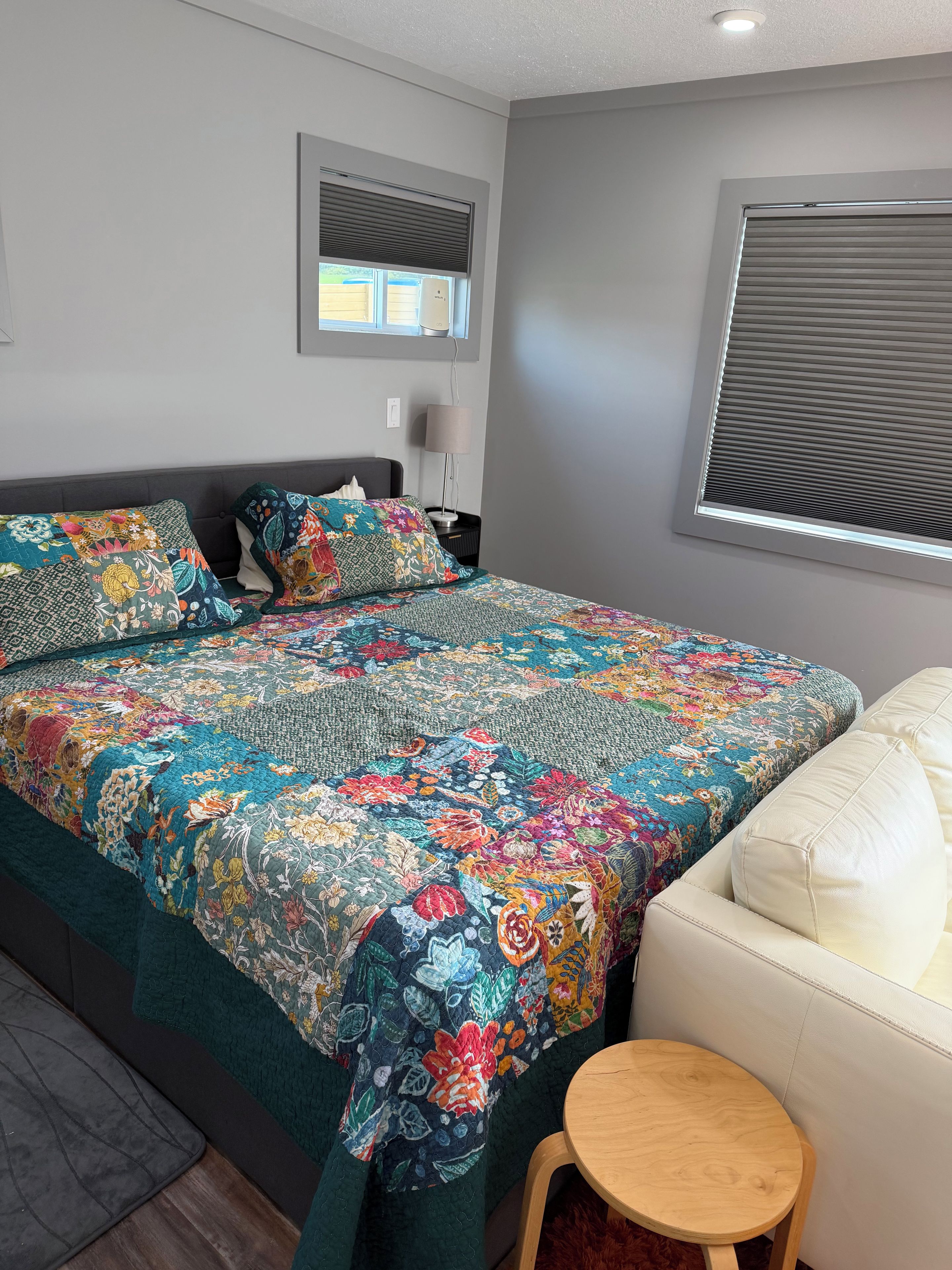 Quarto com cama grande, mesa de cabeceira, abajur e janela com persianas.