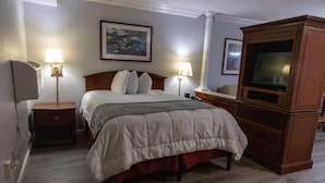 Ein Hotelzimmer mit einem Bett, zwei Nachttischlampen, einem Fernseher und einem gerahmten Bild an der Wand.