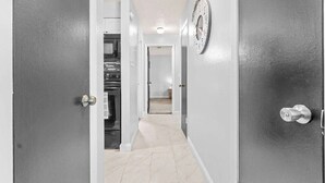 Un pasillo con una zona de cocina, un reloj en la pared y una puerta con pomo de plata.