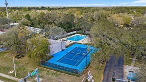Vista aérea de una zona residencial con una gran cancha de tenis azul rodeada de árboles y casas.
