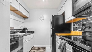 Una cocina compacta con armarios blancos, un refrigerador negro y una estufa.