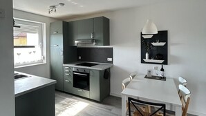Une cuisine moderne avec des meubles gris, une table à manger blanche et un luminaire suspendu.