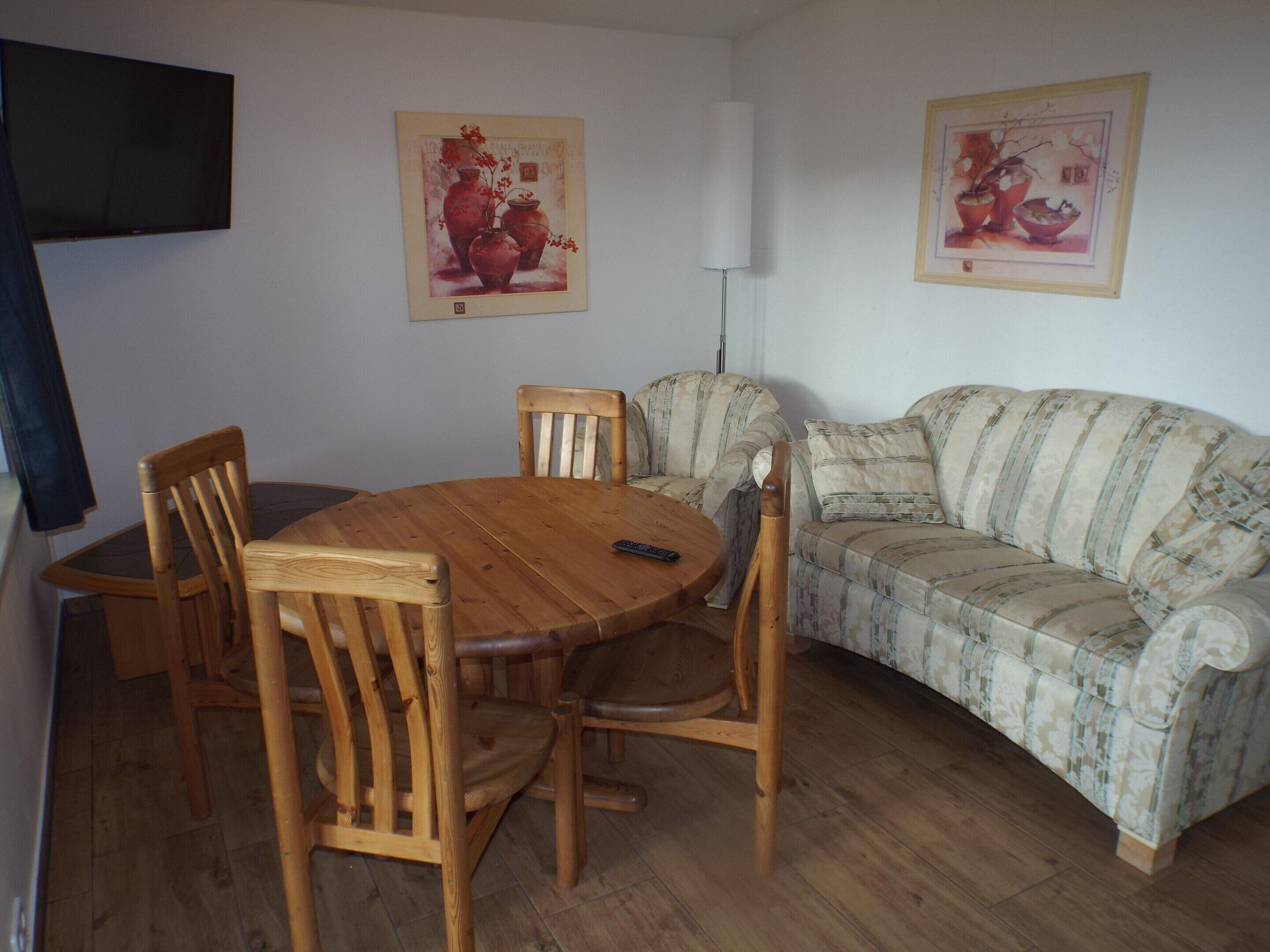 Un salon avec une table ronde en bois, quatre chaises en bois, un canapé et deux œuvres d’art encadrées accrochées au mur.