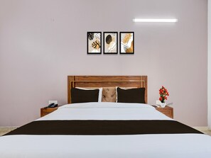 A neatly made bed with a wooden headboard, a bedside table with a phone, and a wall-mounted light fixture. - Hotel O Pari Chowk Metro Station (Greater Noida)