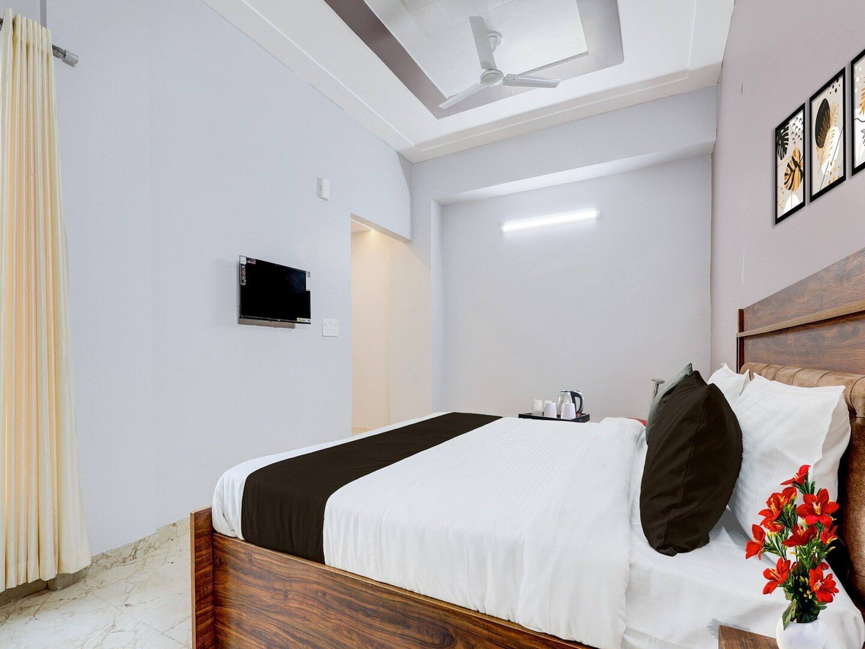 Egy szállodai szoba, amelyben található egy ágy, egy mennyezeti ventilátor, egy síkképernyős televízió, egy éjjeliszemélyzet, rajta egy vízforralóval, és egy virágváz.