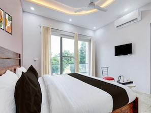 A hotel room with a bed, a TV, an air conditioner, a window with curtains, and a balcony view.