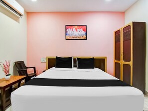 A hotel room with a bed, a desk, a chair, a wardrobe, and a painting on the wall. - Deluxeapex Homestay (Visakhapatnam)