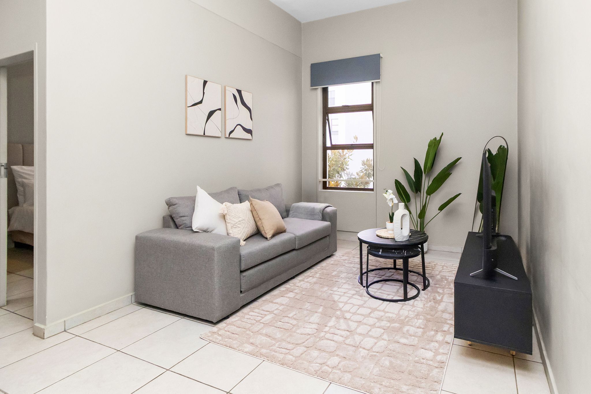 A living room with a grey sofa, a coffee table, a plant, and artwork on the wall.
