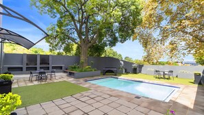 Ein Garten mit Schwimmbad, Terrassenmöbeln und einem Baum.