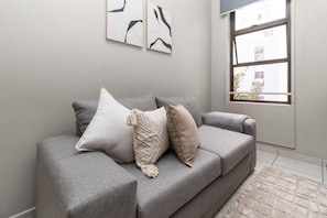 A grey sofa with multiple cushions, a stone-patterned rug, and abstract wall art.