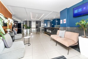 A modern hotel lobby with a reception desk, seating area, and a large screen displaying information. - The Bolton Unit 130 (Johannesburg)