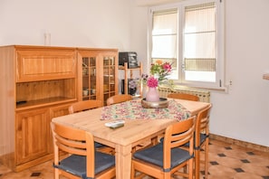 A dining area with a wooden table, chairs, a cabinet, a window with blinds, and a vase with flowers. - Da Nonna Mena (Fossacesia)