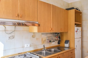 A kitchen with wooden cabinets, a stainless steel range hood, a double sink, and a refrigerator with magnets. - Da Nonna Mena (Fossacesia)