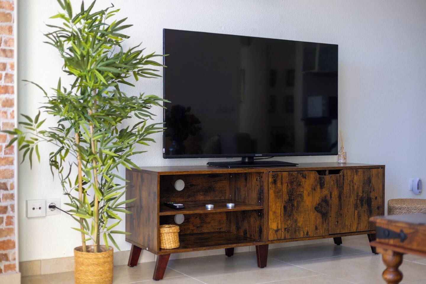 A wooden entertainment center with a flat-screen TV, a potted plant, and a wicker basket.