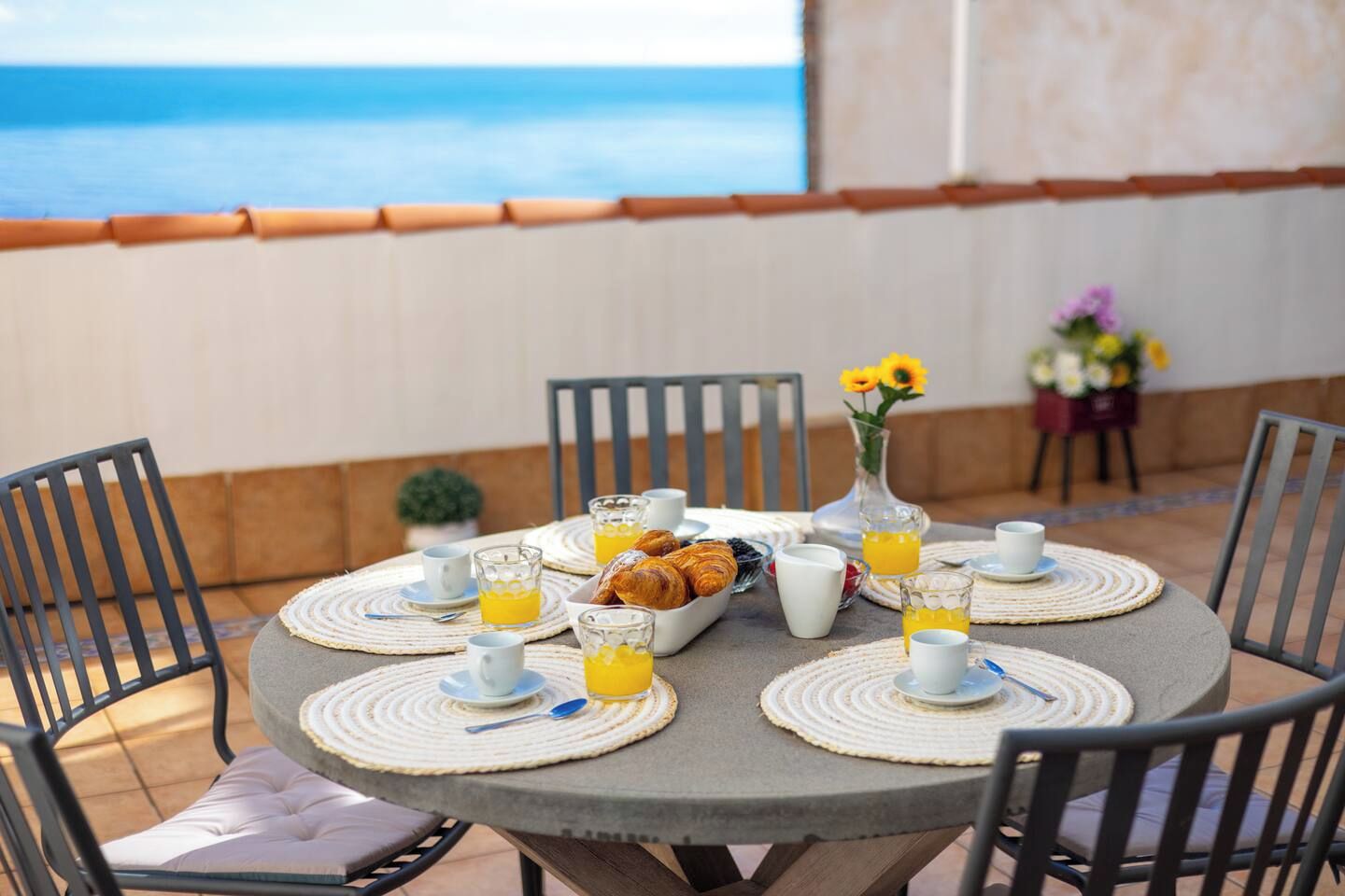 Un tavolo rotondo con una colazione, inclusi croissant, succo d'arancia e tazze di caffè, con vista su un corpo d'acqua.