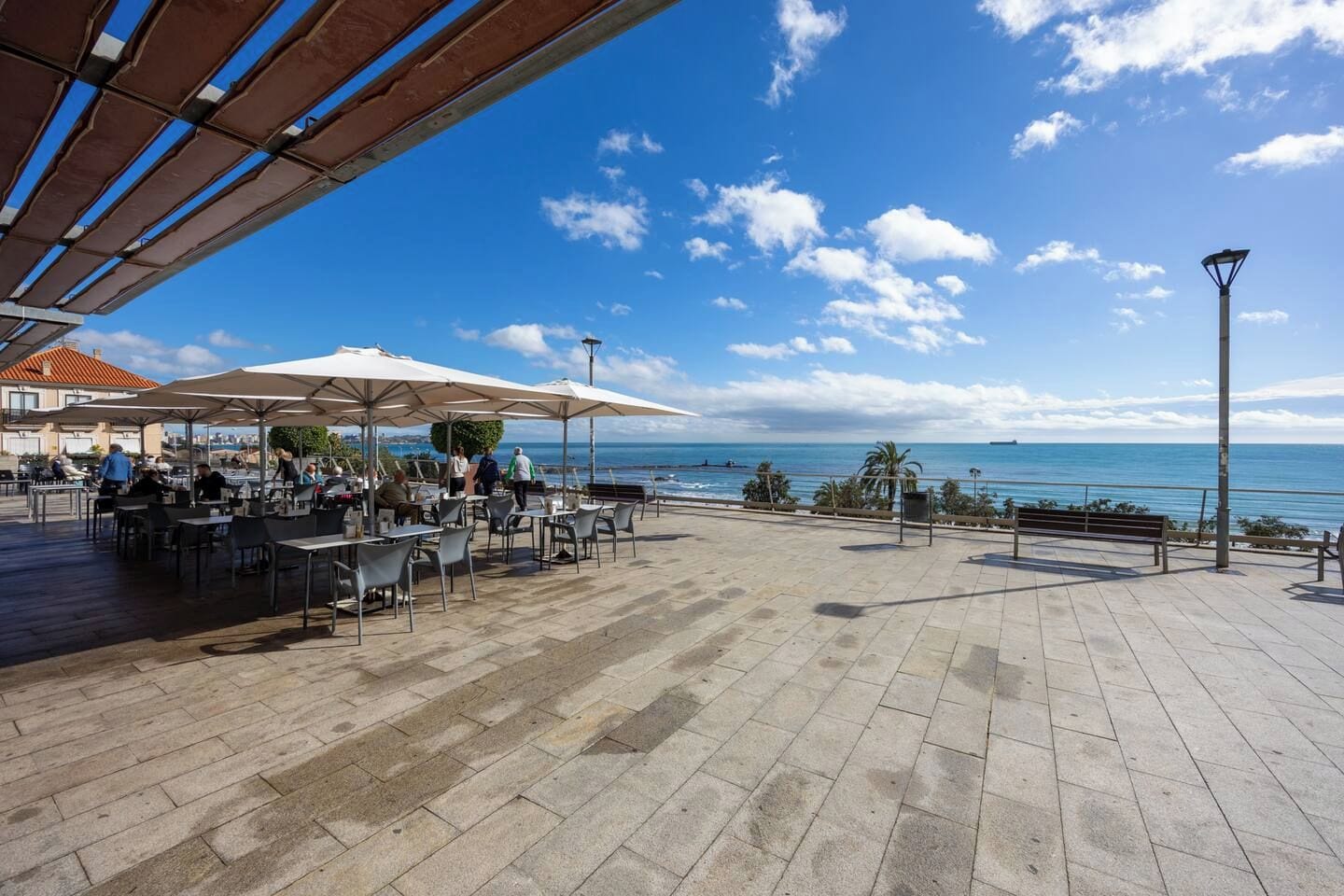 Um café ao ar livre com mesas e guarda-sóis, com vista para a praia e o mar.