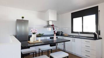 A modern kitchen with a central island, white cabinetry, a stainless steel range hood, and a window with a black frame.