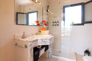 Un baño con lavamanos de mármol, cabina de ducha de vidrio y un inodoro.