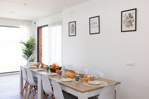 A dining area with a long table set for breakfast, white chairs, and framed artwork on the walls.