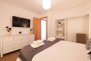 Une chambre à coucher comprenant un lit, une télévision, une armoire et une porte donnant sur une autre pièce.