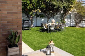 Un patio trasero cuidado con zona de comedor, una parrilla y una planta en maceta.