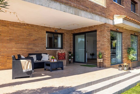 Une maison moderne avec une façade en briques, un patio couvert aménagé avec du mobilier et une porte-fenêtre coulissante donnant sur un espace intérieur.