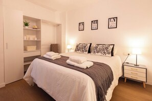 Una habitación de hotel con una cama, mesitas de noche, un armario y almohadones decorativos.