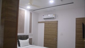 A bedroom with a bed, a wardrobe, an air conditioning unit, and a ceiling fan. - The Ramayan (Orchha)