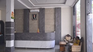 A reception area with a marble reception desk, a framed portrait on the wall, and a seating area with patterned chairs. - The Ramayan (Orchha)