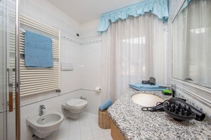 A bathroom with a sink, bidet, and toilet, a towel rack, and a mirror.