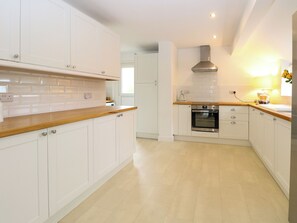 A modern kitchen with white cabinetry, a wooden countertop, a built-in oven, and a stainless steel range hood. - Three Ways (Diss)