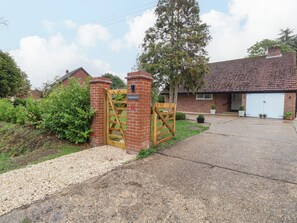 A gated entrance to a property with a brick wall, a wooden gate, and a paved driveway leading to a garage. - Three Ways (Diss)