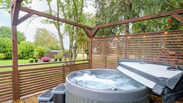 Banyera d'hidromassatge sota una pérgola de fusta amb vista a un jardí.