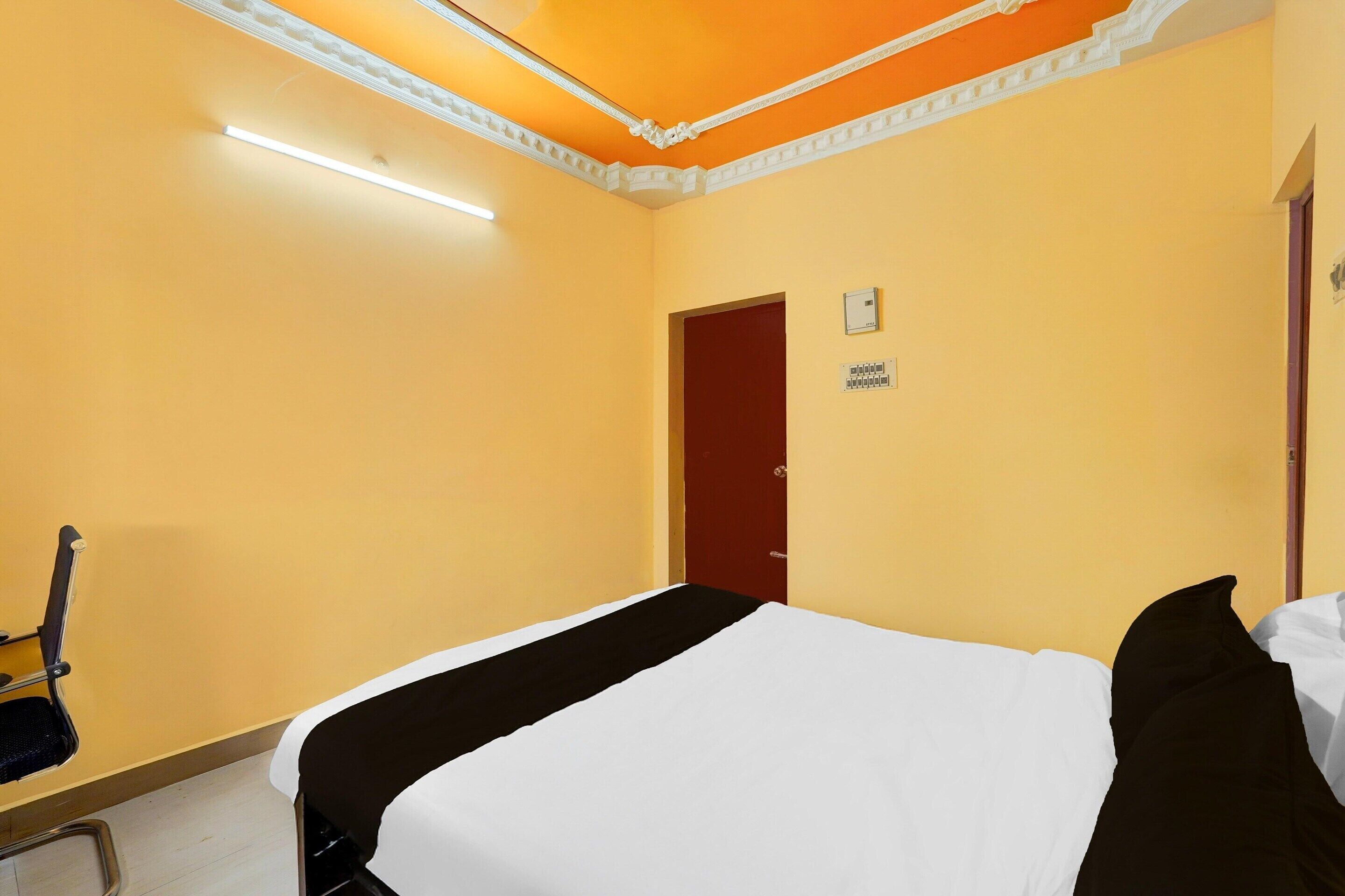 A hotel room with a bed, a chair, a door, and a light fixture.