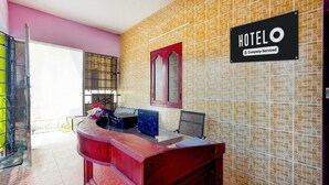 Un mostrador de recepción de hotel con un cartel de la empresa, una pared con diseño y una puerta con reja de metal.