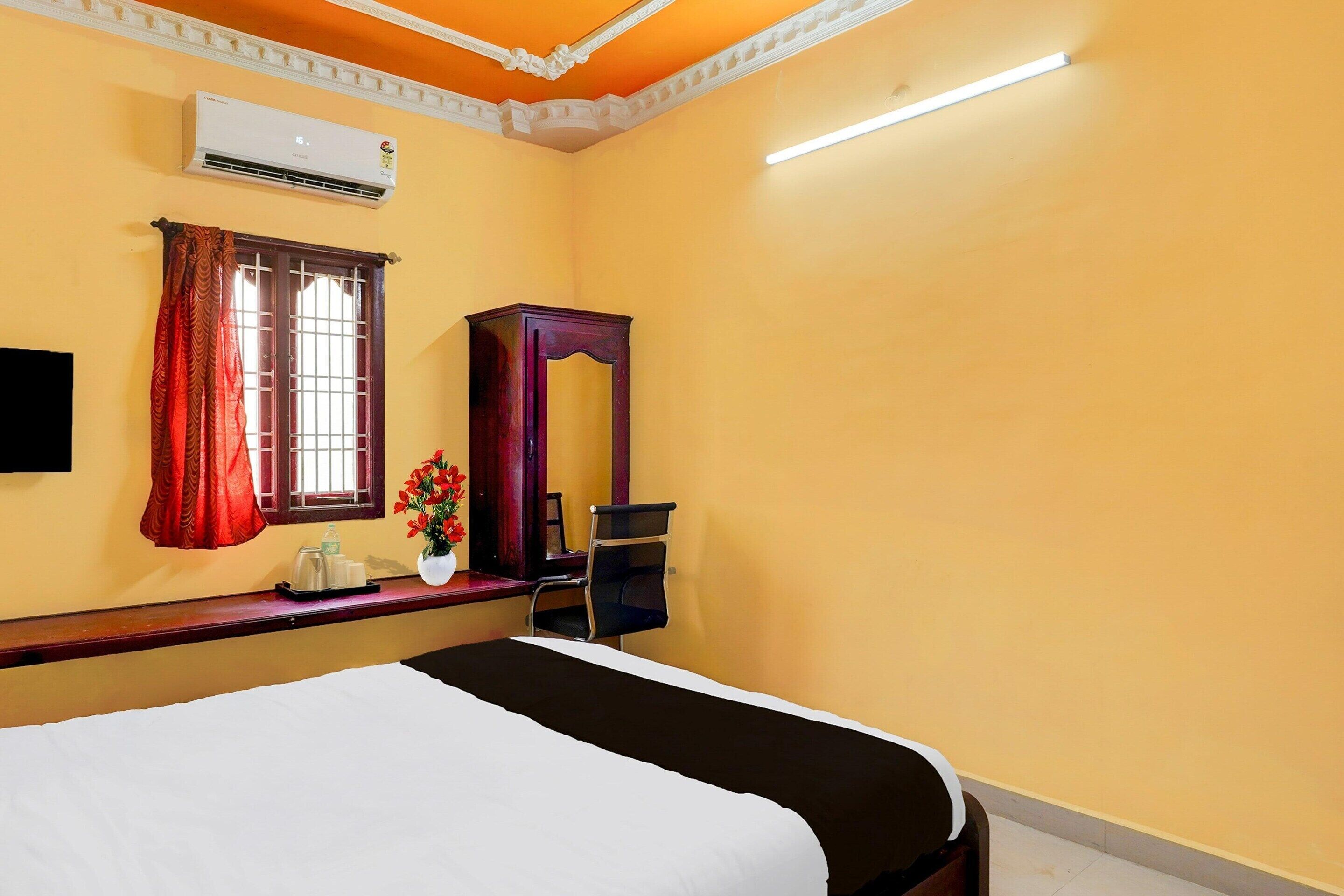 Habitación de hotel con cama, escritorio, silla, equipo de aire acondicionado y ventana con cortinas.
