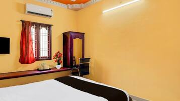 Habitación de hotel con cama, escritorio, silla, equipo de aire acondicionado y ventana con cortinas.