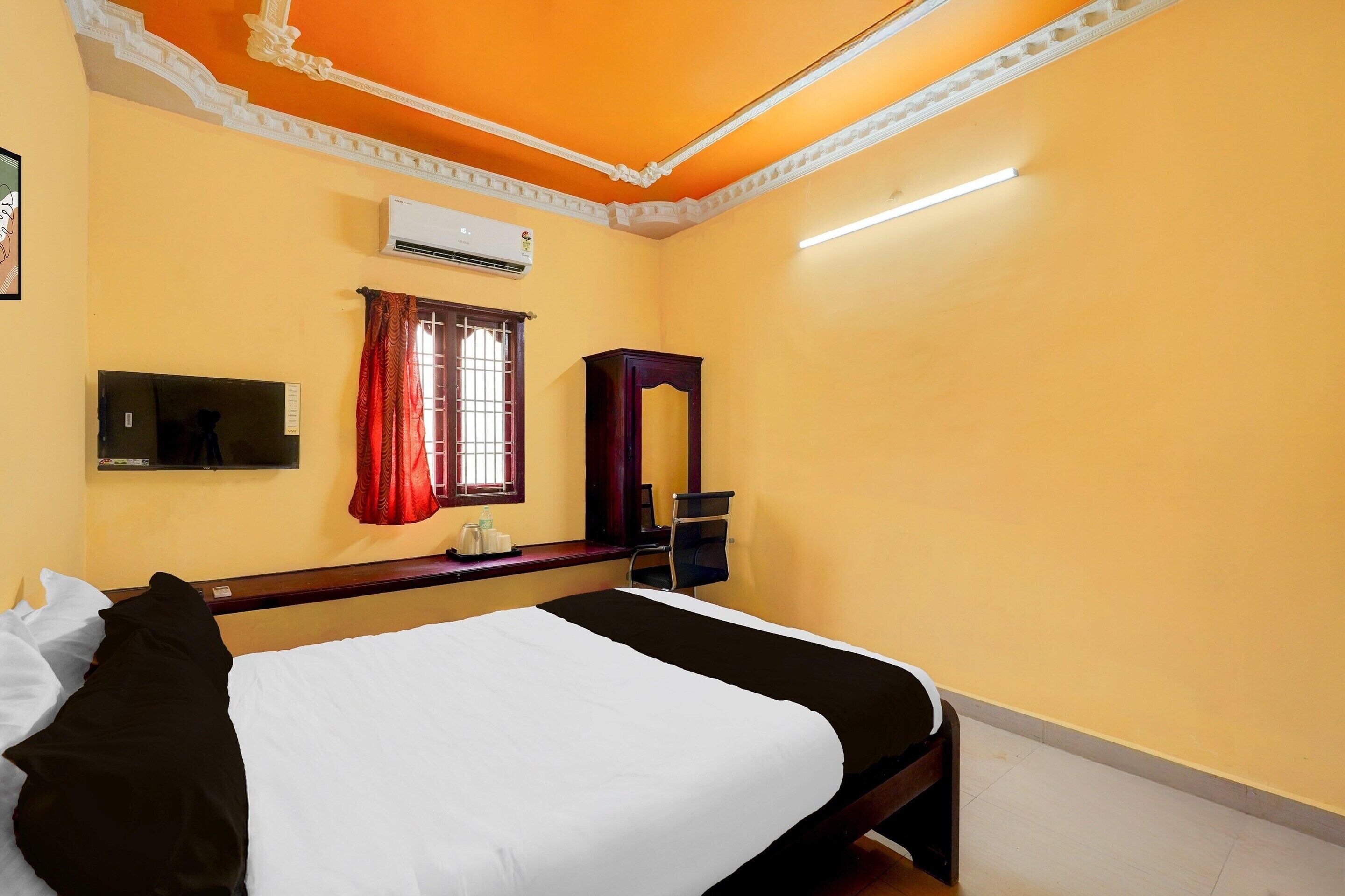 Habitación de hotel con cama, escritorio, aire acondicionado, ventana con cortinas y espejo.