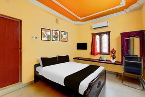 Habitación de hotel con cama, escritorio, silla, aire acondicionado y ventana con cortinas.