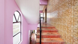 Una escalera con peldaños rojos que lleva a una plataforma, una pared rosa y un papel tapiz estampado a la derecha.