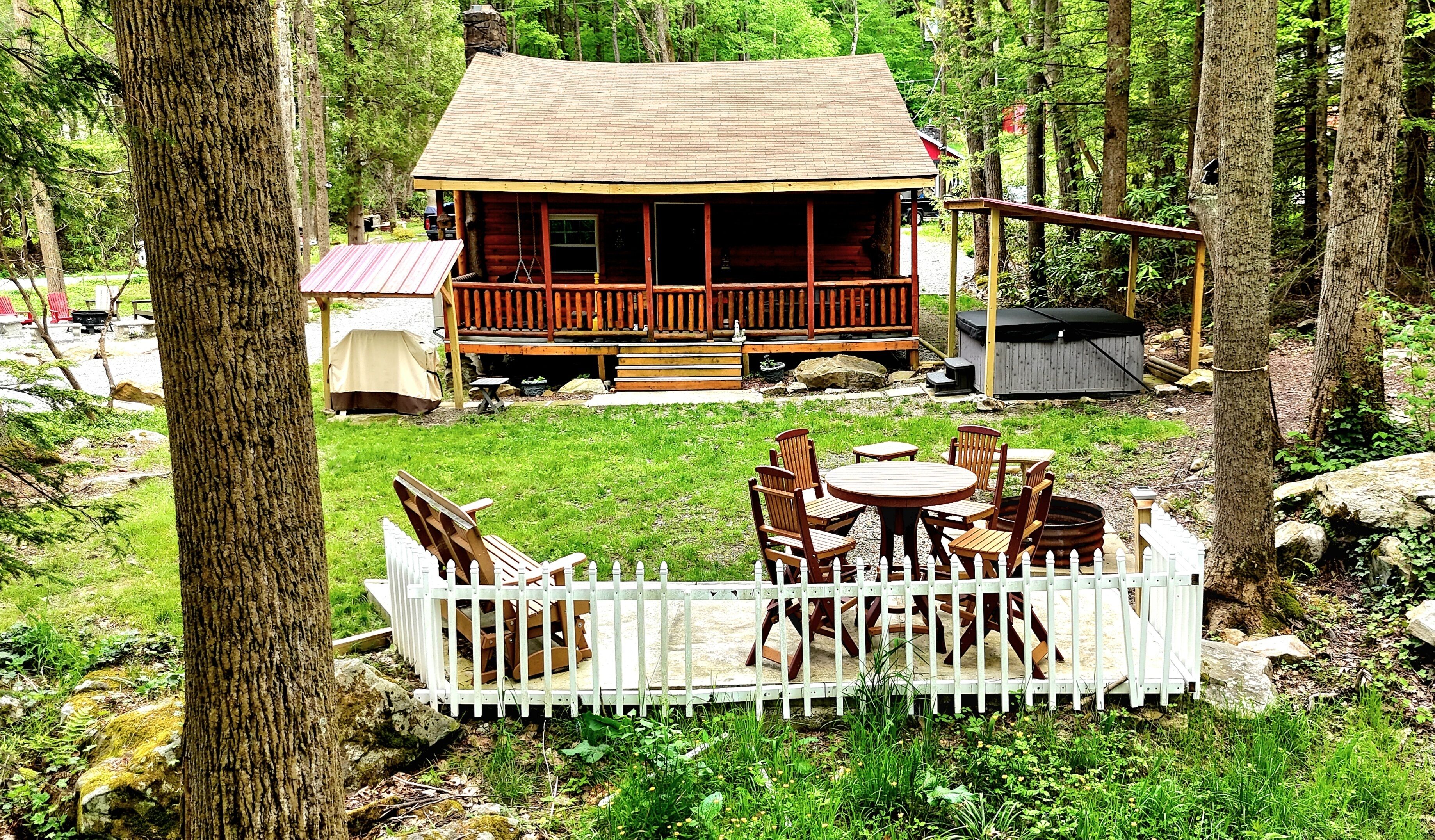 Une cabane dotée d’une terrasse, entourée d’une clôture en bois peinte en blanc, et comprenant un espace salon extérieur.