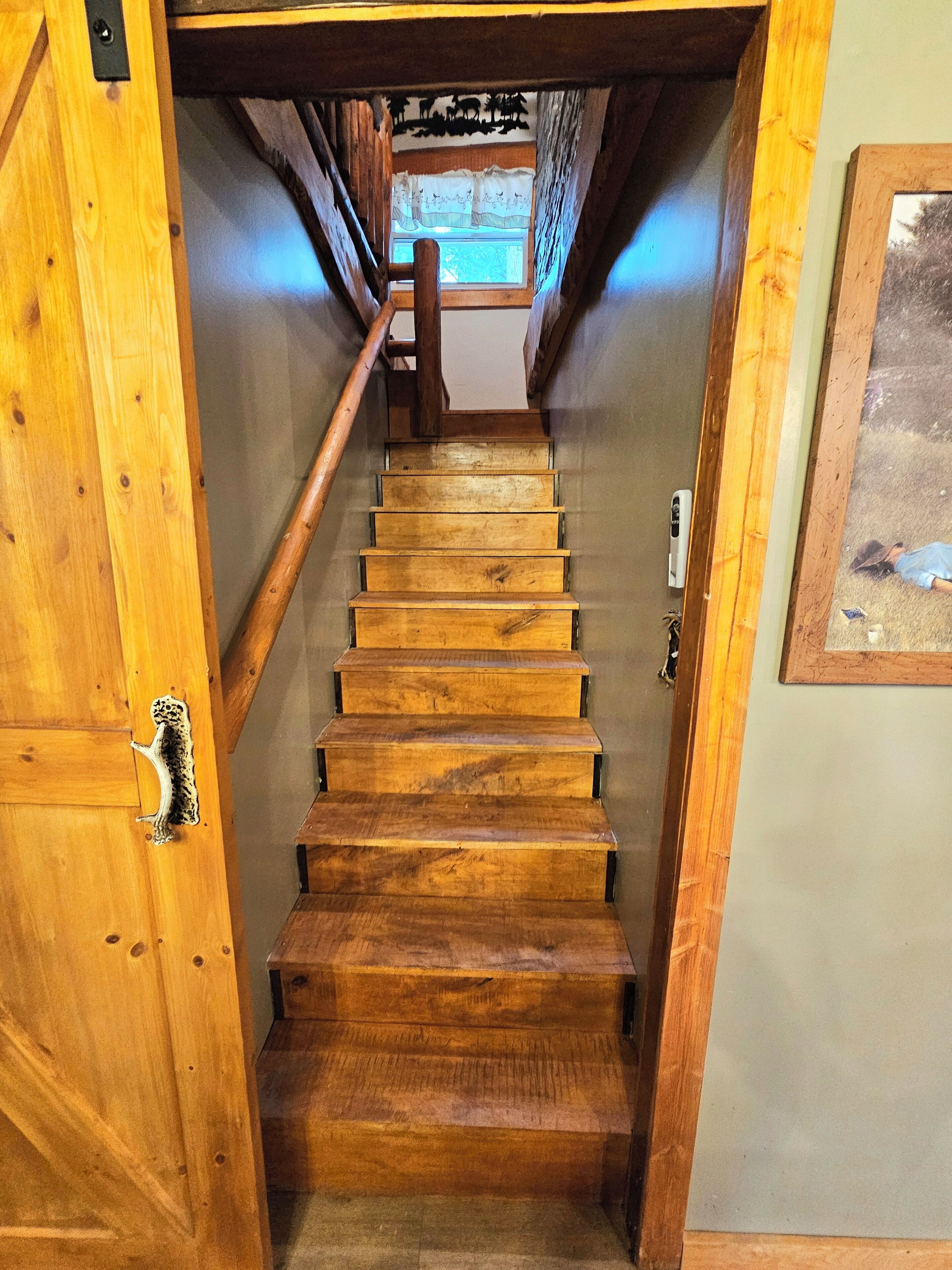 Un escalier en bois menant à l’étage supérieur, avec vue sur l’extérieur par une fenêtre.
